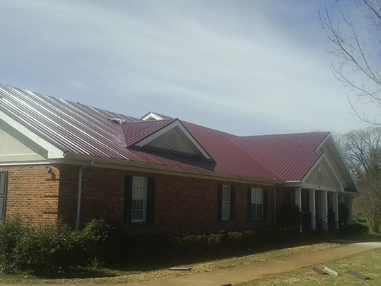 Red metal roof with gabled entries on a long brick building, from a Hail Damage Roof Repair job in Honesdale