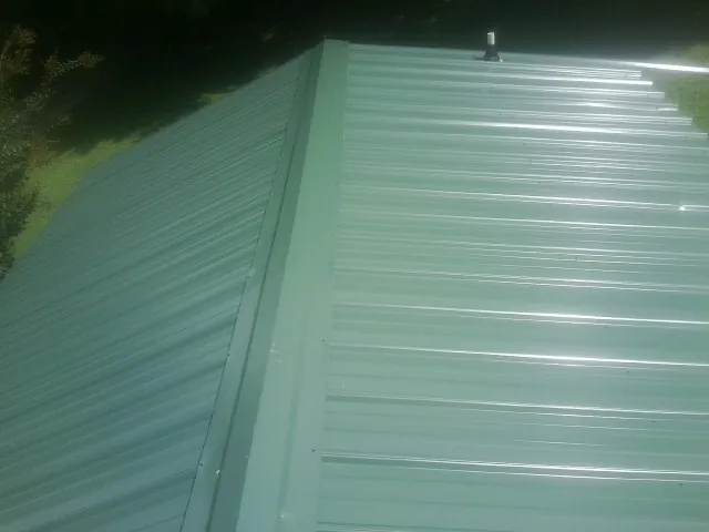 New green metal panels meeting at the ridge of a roof — Flat Roof Repair work by our crew in Honesdale
