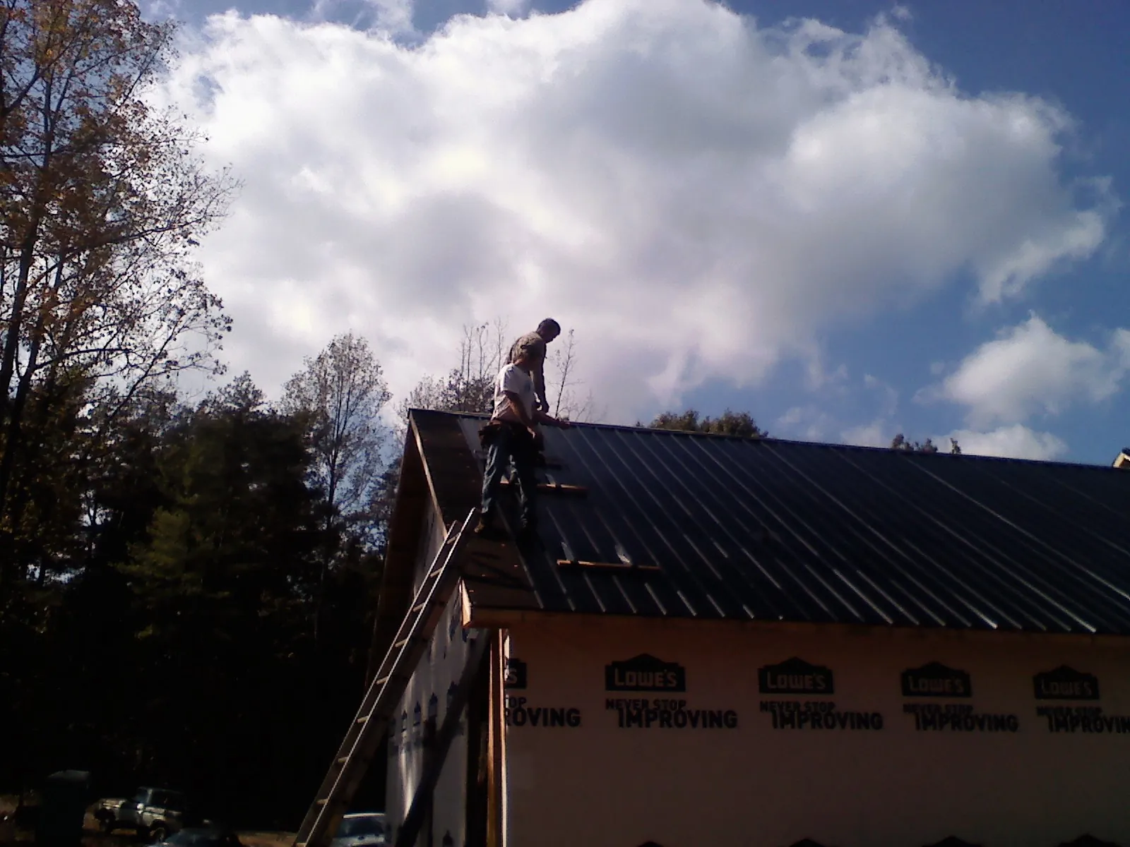 Roofer fastening dark metal panels high against a cloudy sky, from a Roof Inspection job in Honesdale
