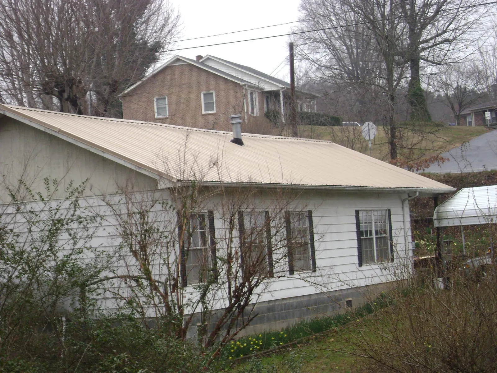 Tan metal roof on a white sided house set into a hillside — Commercial Roofing by Roofing Brothers in Honesdale
